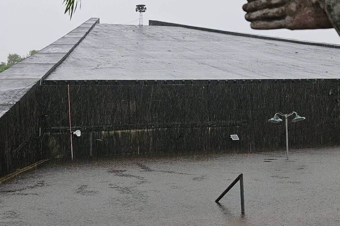 Floodwater in Bacolor risen almost to the roofline of a building, with a basketball ring and a lamppost half submerged in heavy rain.