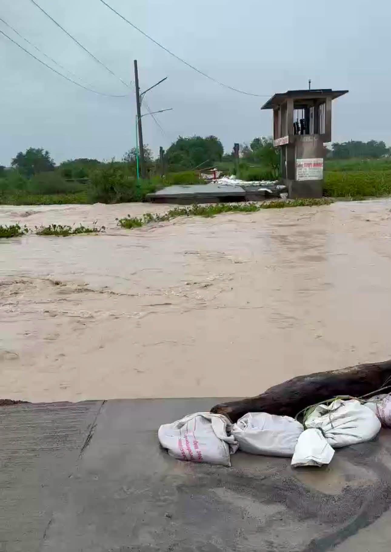 Fast muddy water pours through a breached section of the tail dike in Barangay Santa Catalina, Minalin, despite sandbags along the remaining pavement.